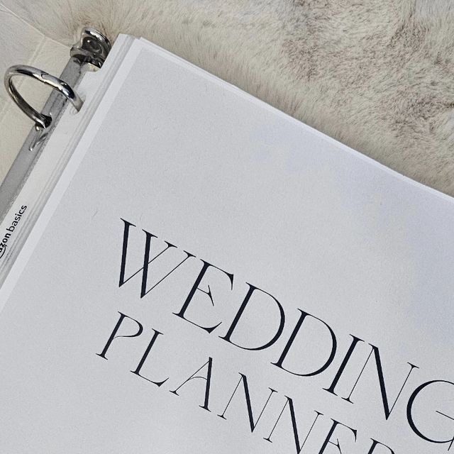 Close-up of a wedding planner binder labeled "Wedding Planner" resting on a desk. The binder is neatly organized and ready to help couples stay on track with wedding planning, making it an essential tool for brides and grooms organizing their big day.